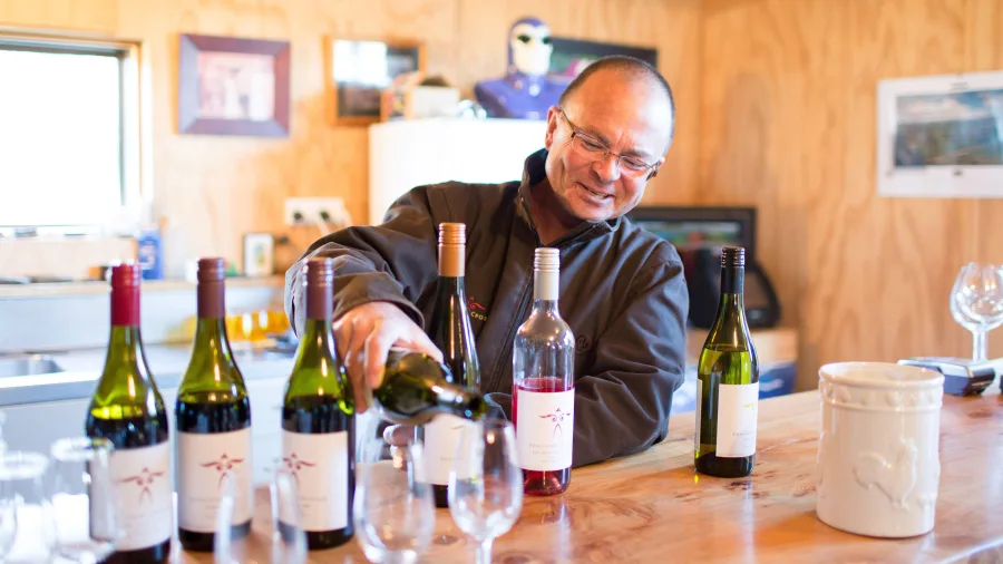 Smiling winemaker pouring wine during a tasting at Swallows Crossing Vineyard near Wanaka.