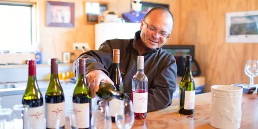 Smiling winemaker pouring wine during a tasting at Swallows Crossing Vineyard near Wanaka.