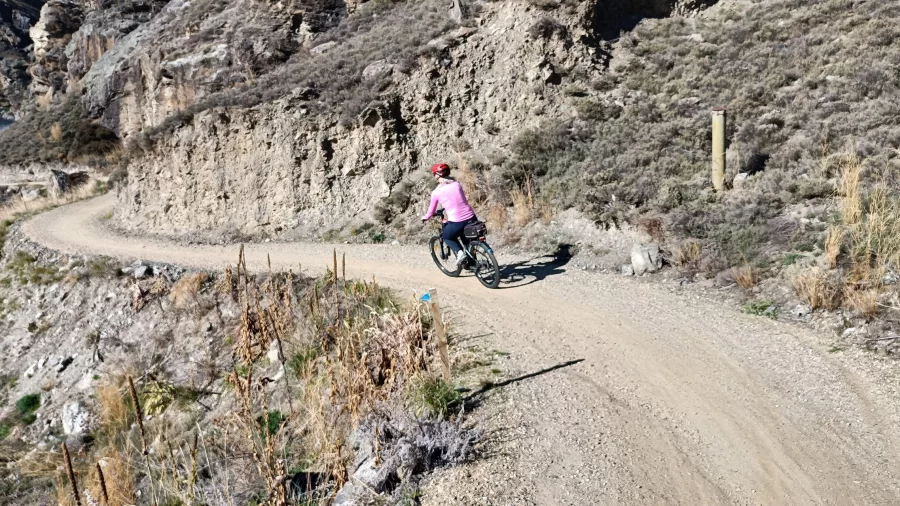 Cyclist on a winding gravel section of the Lake Dunstan Trail surrounded by rocky terrain.