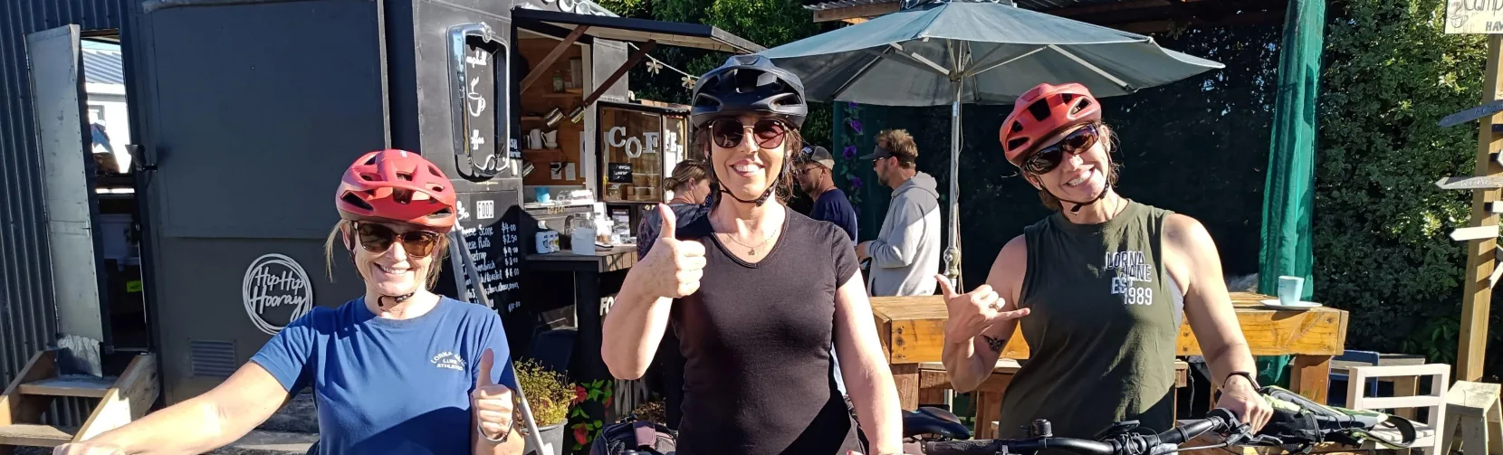 Group of smiling cyclists stopping for coffee at a local café in Hawea Flat.