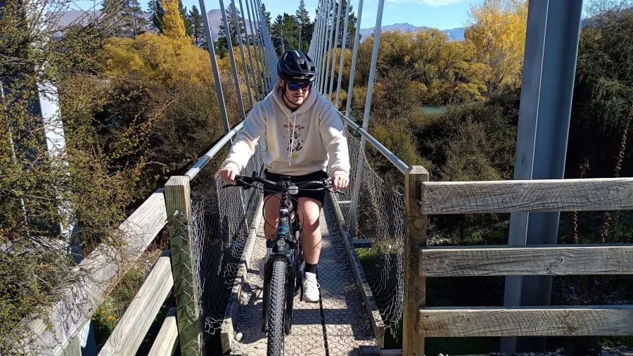 Cyclist crossing the Albert Town swing bridge over the Hawea River near Wanaka.