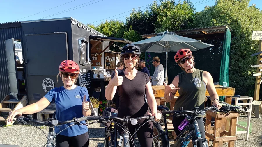 Group of smiling cyclists stopping for coffee at a local café in Hawea Flat.