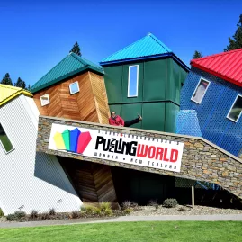 Exterior of Puzzling World in Wānaka featuring colourful tilted buildings and a visitor posing on the ramp