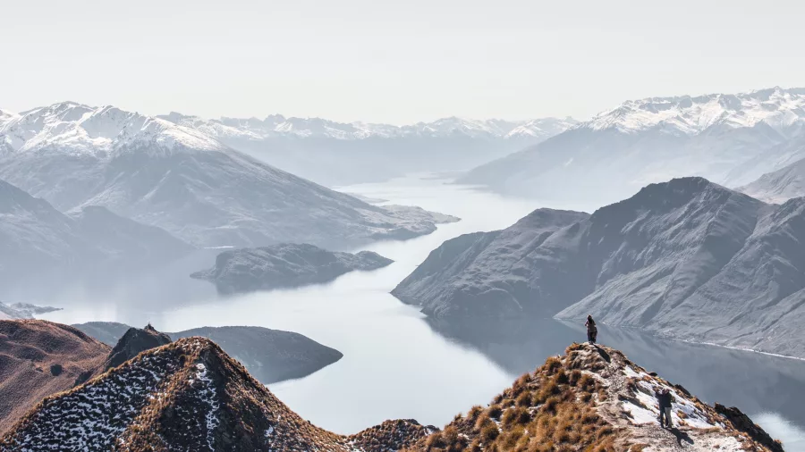 Hikers standing on Roys Peak with panoramic views of Lake Wānaka and snow-capped mountains