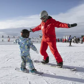 Child learning to snowboard with an instructor at Cardrona Alpine Resort in New Zealand
