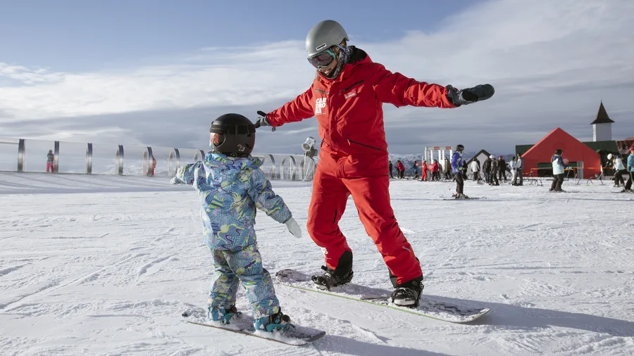 Child learning to snowboard with an instructor at Cardrona Alpine Resort in New Zealand
