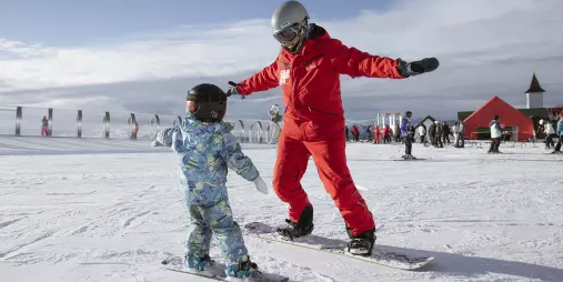 Child learning to snowboard with an instructor at Cardrona Alpine Resort in New Zealand