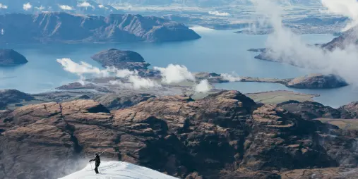 Solo skier on snowy summit at Treble Cone with panoramic view over Lake Wānaka and islands
