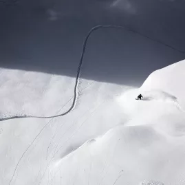 Lone skier or snowboarder carving a single track through untouched backcountry snow in the mountains near Wānaka, New Zealand
