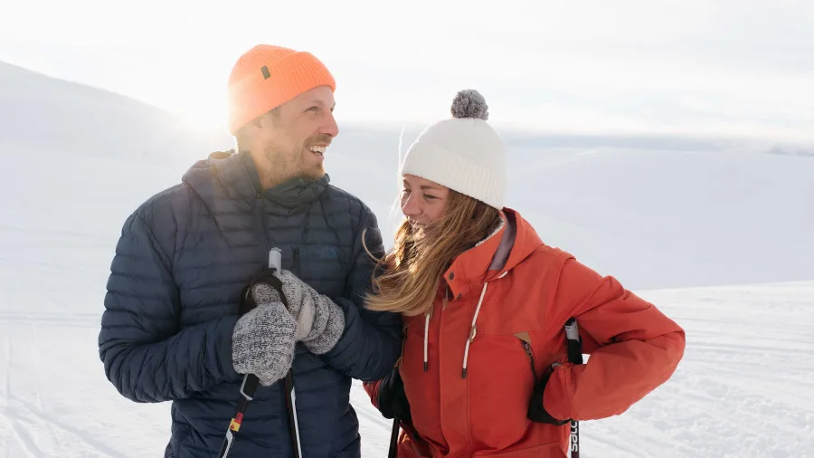 Happy couple holding ski poles against snowy alpine backdrop in Wānaka winter