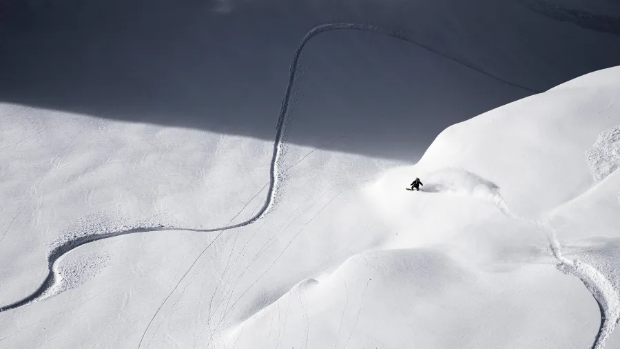Lone skier or snowboarder carving a single track through untouched backcountry snow in the mountains near Wānaka, New Zealand