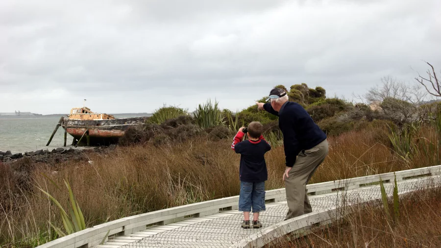Grandfather and child pointing at old shipwreck on Greenpoint Walkway