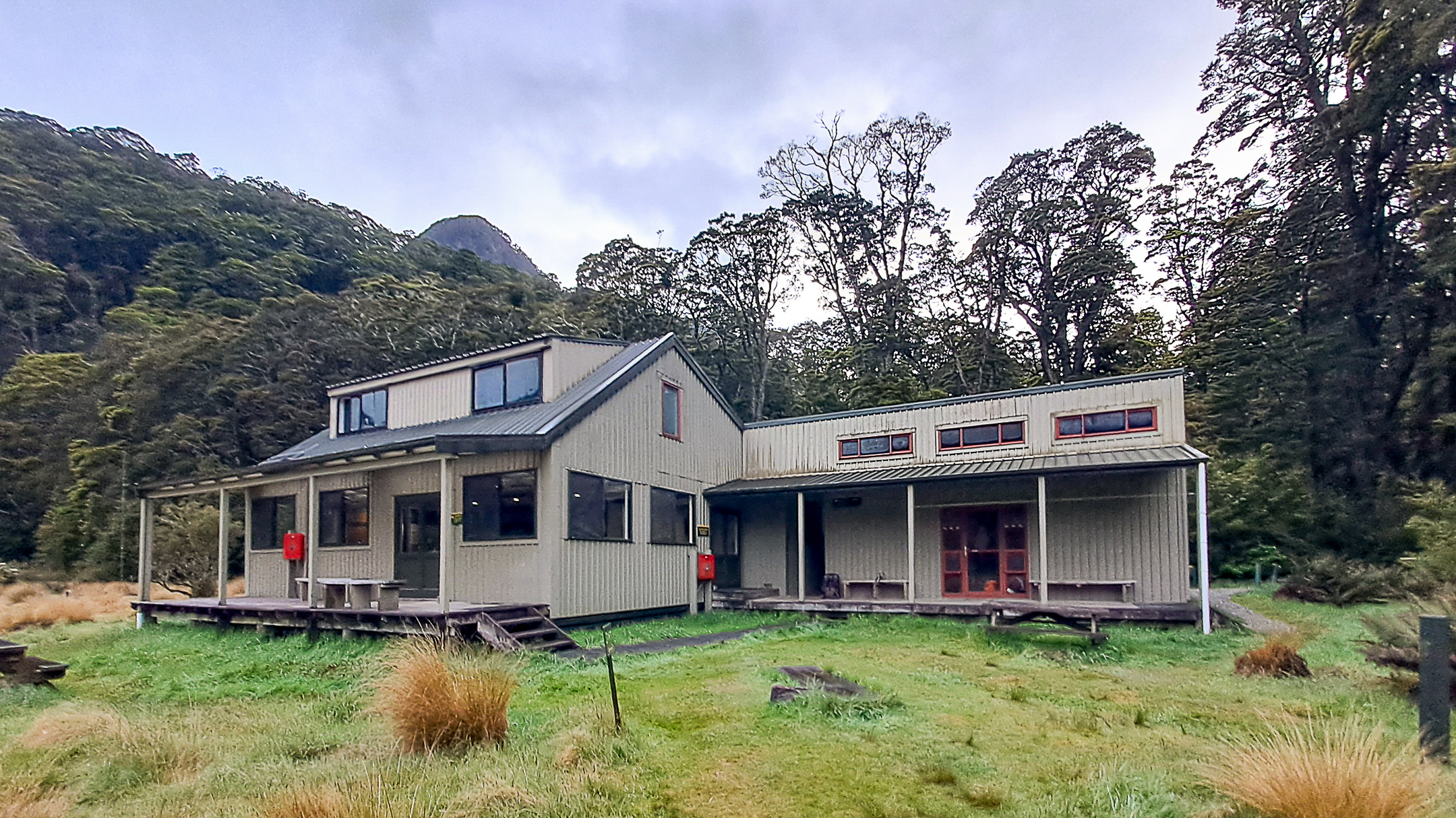 Exterior of Iris Burn Hut on the Kepler Track, surrounded by trees and mountains under an overcast sky.