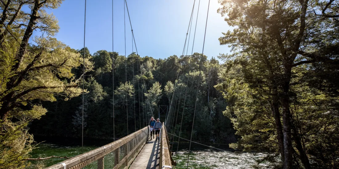 Hikers crossing the swing bridge over the Waiau River on the Kepler Track, Southland, New Zealand
