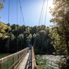 Hikers crossing the swing bridge over the Waiau River on the Kepler Track, Southland, New Zealand