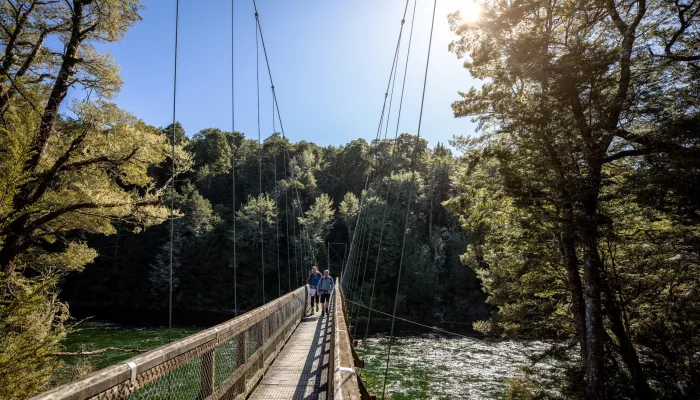 Hikers crossing the swing bridge over the Waiau River on the Kepler Track, Southland, New Zealand