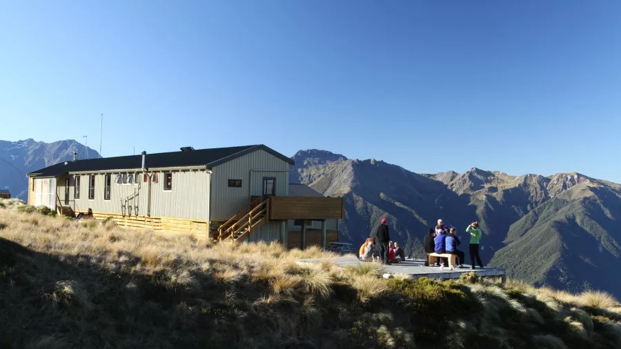 Hikers resting outside Luxmore Hut on the Kepler Track with alpine mountain views