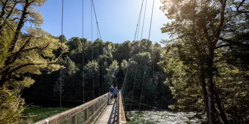 Hikers crossing the swing bridge over the Waiau River on the Kepler Track, Southland, New Zealand