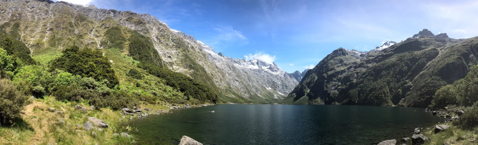 Panoramic view of Lake Marian surrounded by snow-capped mountains in Fiordland National Park, Southland New Zealand