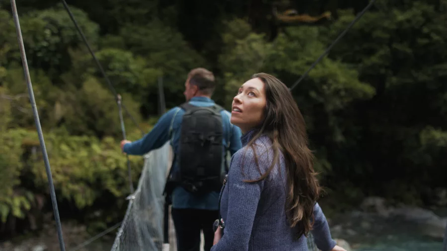 Hikers crossing swing bridge surrounded by native bush on the Lake Marian Track, Southland New Zealand