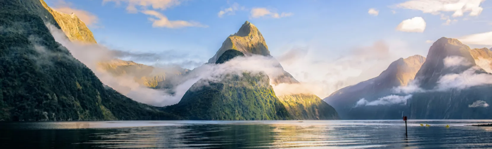 Scenic view of Mitre Peak rising above the calm waters of Milford Sound surrounded by mist and mountains in Fiordland National Park, New Zealand