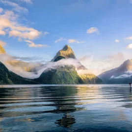 Scenic view of Mitre Peak rising above the calm waters of Milford Sound surrounded by mist and mountains in Fiordland National Park, New Zealand