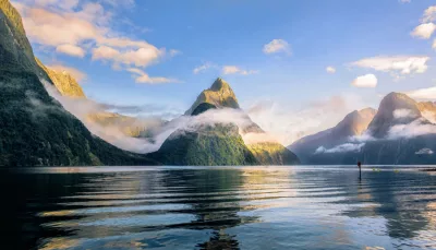 Scenic view of Mitre Peak rising above the calm waters of Milford Sound surrounded by mist and mountains in Fiordland National Park, New Zealand