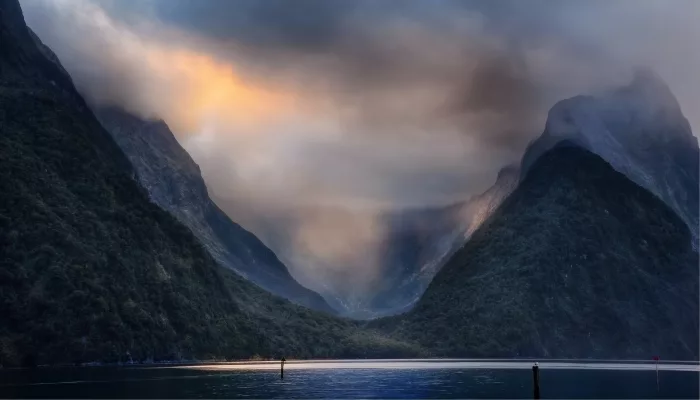 Golden sunrise light filtering through clouds over Milford Sound Piopiotahi, Fiordland National Park, New Zealand