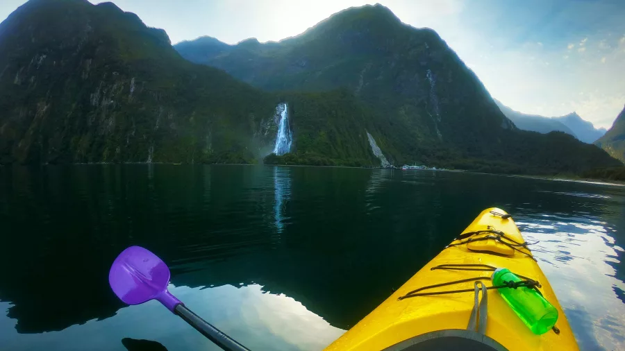 Kayaker paddling towards Bowen Falls at Milford Sound Piopiotahi, Fiordland National Park, New Zealand