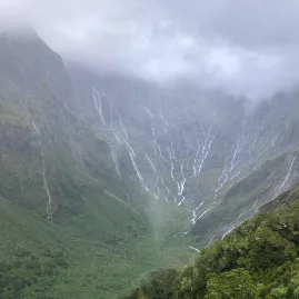 Waterfalls cascading down the valley walls on a rainy day along the Milford Track, New Zealand