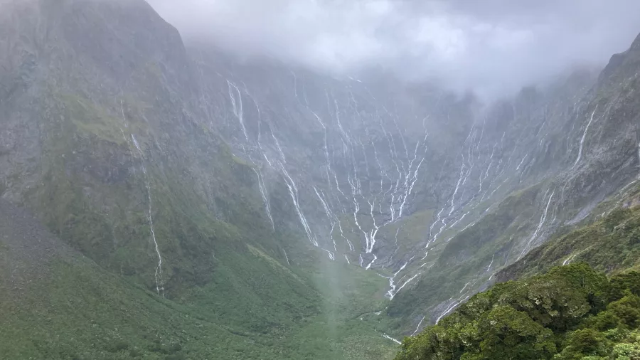Waterfalls cascading down the valley walls on a rainy day along the Milford Track, New Zealand