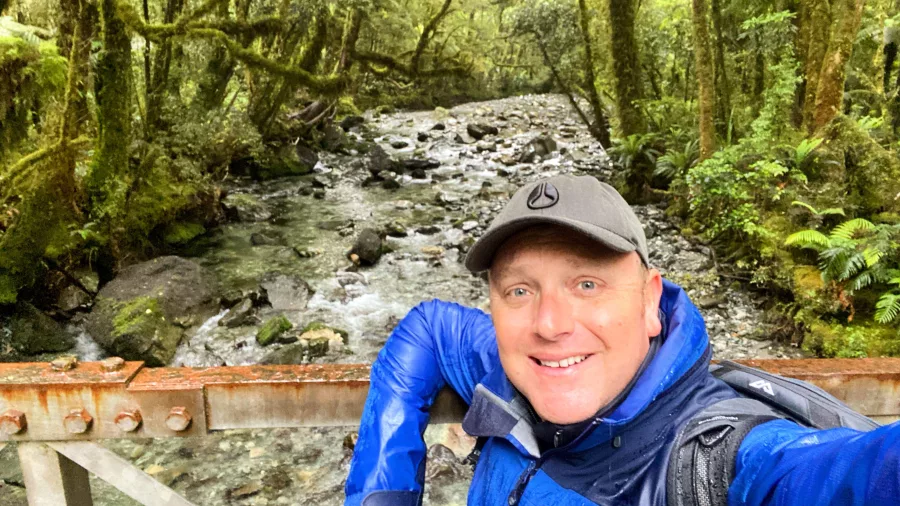 Hiker taking a selfie on a bridge over a stream on the Milford Track, Southland New Zealand