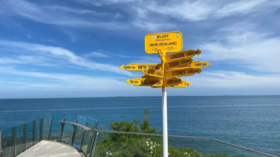 Scenic viewpoint at Bluff with a yellow signpost showing distances to cities like London and New York.