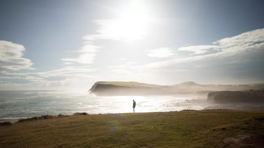 Person standing on windswept Curio Bay headland in the Catlins, Southland, under bright sunlight.