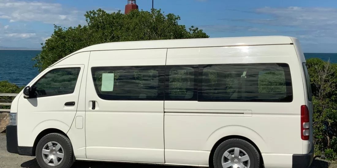 White Catch a Bus South shuttle van parked with a coastal view near Invercargill.