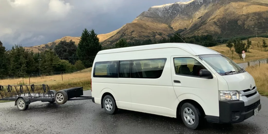 Catch a Bus South transfer van with luggage trailer parked on a scenic Southland road near Invercargill.