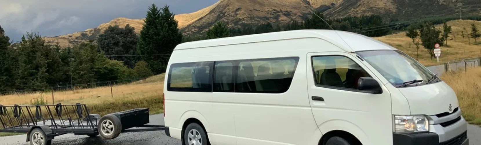 Catch a Bus South transfer van with luggage trailer parked on a scenic Southland road near Invercargill.