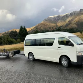 Catch a Bus South transfer van with luggage trailer parked on a scenic Southland road near Invercargill.