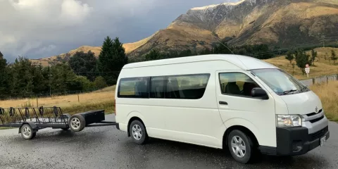 Catch a Bus South transfer van with luggage trailer parked on a scenic Southland road near Invercargill.