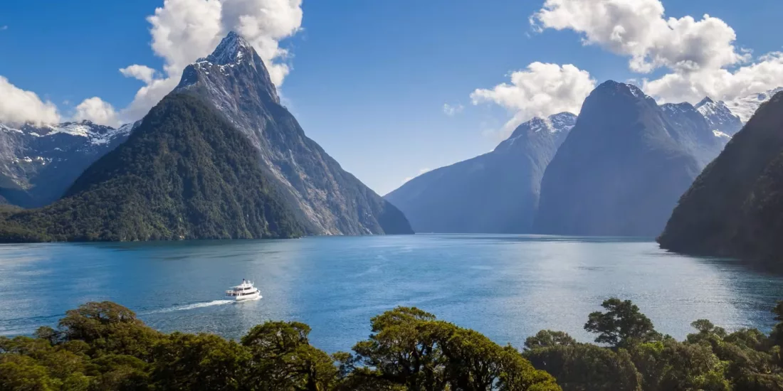 Cruise boat sailing through Milford Sound with Mitre Peak and dramatic fiord scenery