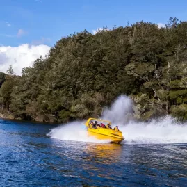 Yellow jet boat speeding through the Waiau River near Lake Manapouri, creating a splash.