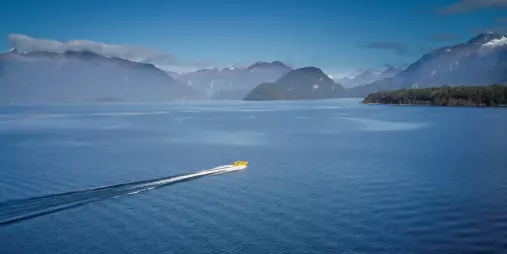 Jet boat gliding across the vast waters of Lake Manapouri with Fiordland mountains in the distance.