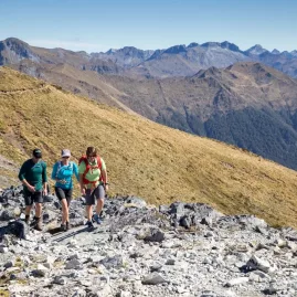 Three hikers walking along an alpine section of the Kepler Track near Luxmore Hut.