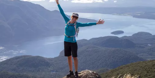 Woman celebrating at the summit with Lake Te Anau and mountains in the background.