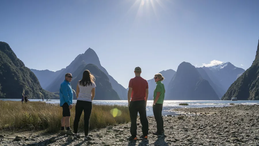 Group enjoying sunshine and views on the shoreline of Milford Sound.