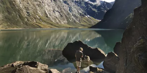 Hiker admires the mirror-like reflection of mountains at Lake Marian on a guided walk from Te Anau.