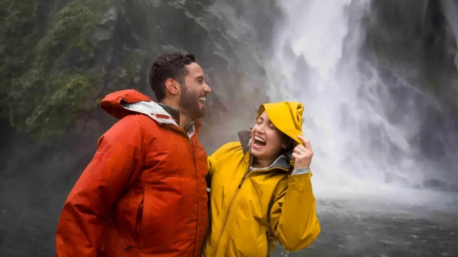 Couple laughing in colourful rain jackets while getting sprayed near Stirling Falls on a Milford Sound nature cruise.
