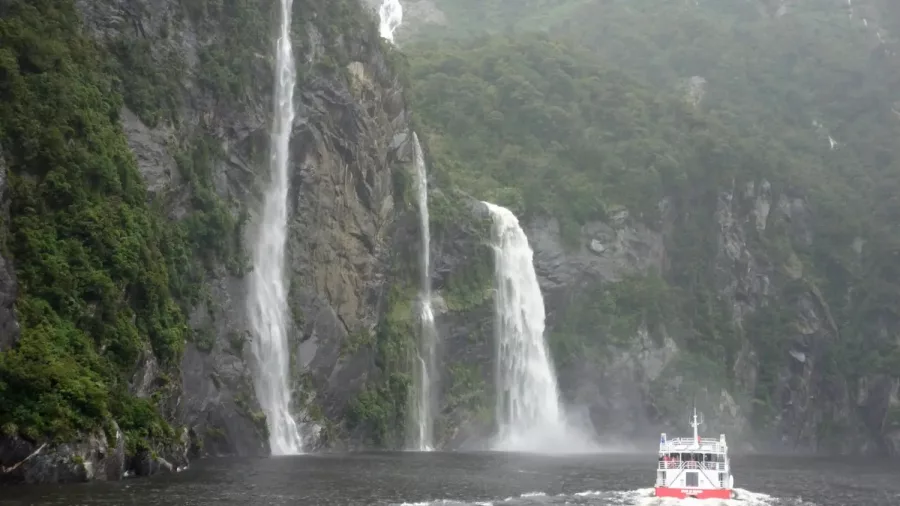 Southern Discoveries cruise boat approaches Stirling Falls in Milford Sound on a misty day.