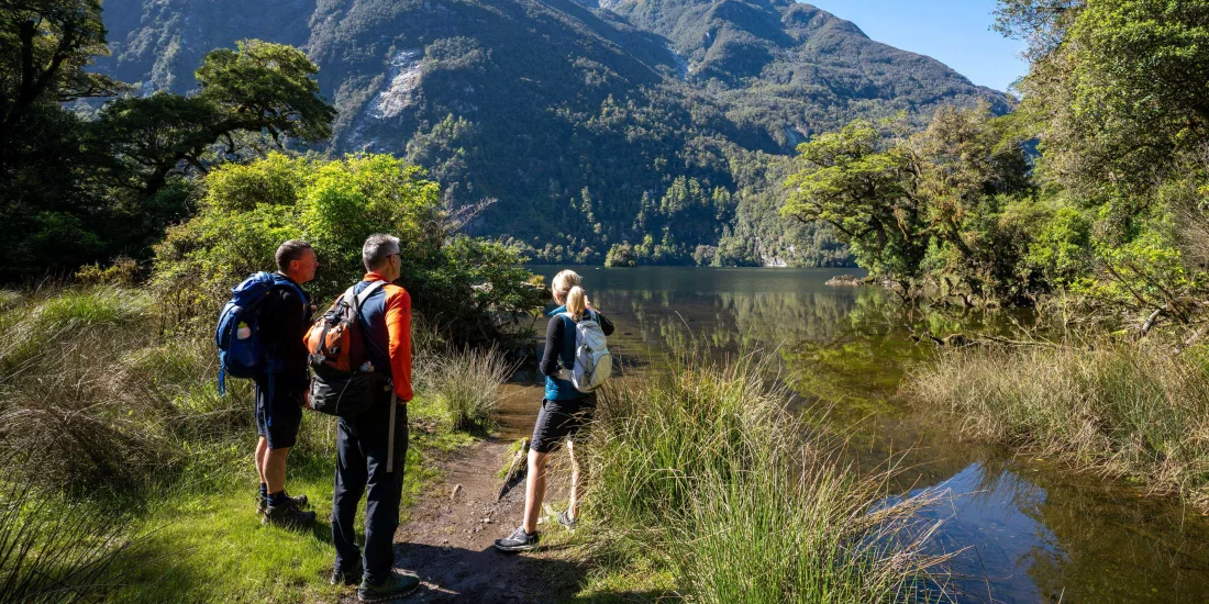 Walkers pause beside Lake Ada with dramatic mountain peaks towering in the distance.