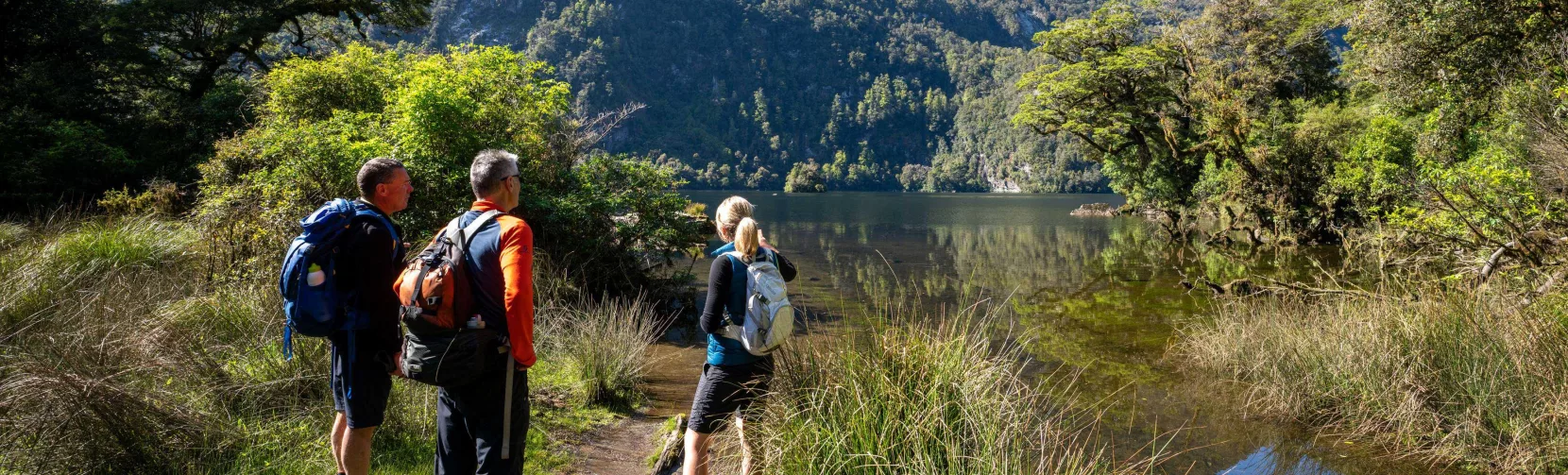 Walkers pause beside Lake Ada with dramatic mountain peaks towering in the distance.